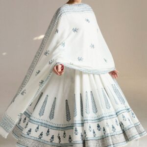 The selected region features a traditional Zara Shahjahan off-white cotton anarkali ensemble decorated with intricate blue hand-block floral motifs. The outfit highlights classic Pakistani ethnic wear styling, pairing a heavily flared floor-length anarkali kurta with a matching block-printed dupatta and tight-fitting churidar pants.Outfit BreakdownKurta: Multi-paneled (kalidar) tiered silhouette with traditional Mughal block printing along the lower border panels.Dupatta: Pure kora cotton with delicate border lining and small block-printed floral sprays throughout.Footwear: Accented with embellished metallic silver juttis or khussas.